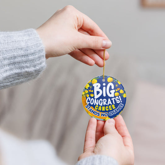 Cancer Victory Ceramic Ornament. Round blue and yellow sticker with 'Big Congrats! Cancer Stands No Chance' text held by two hands against a neutral background.