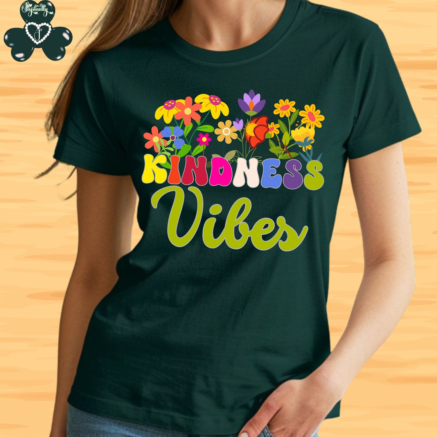 Motivational T-shirt for positive affirmations. Person wearing a dark green t-shirt with colorful floral design and 'Kindness Vibes' text on a wooden surface.