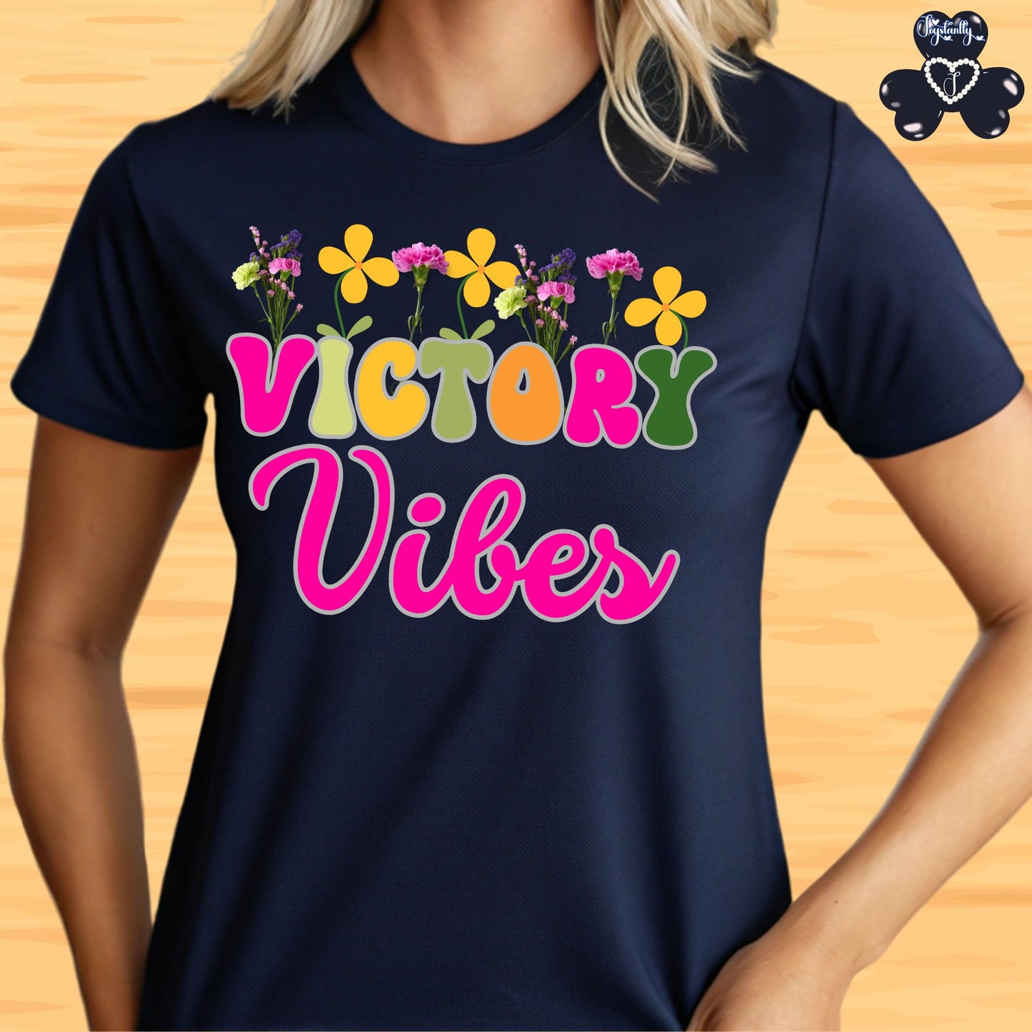 Motivational T-shirt for positive affirmations. Navy blue t-shirt with 'Victory Vibes' text and colorful flowers on a wooden surface