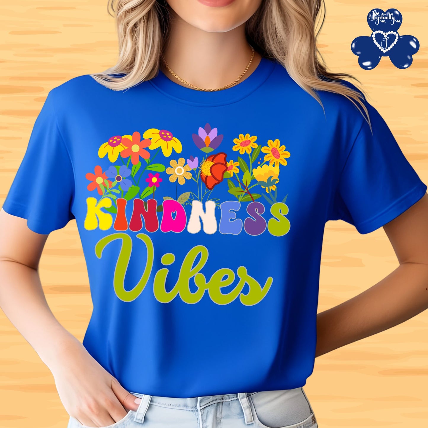 Motivational T-shirt for positive affirmations. Person wearing a blue t-shirt with colorful floral design and 'Kindness Vibes' text on a wooden background.