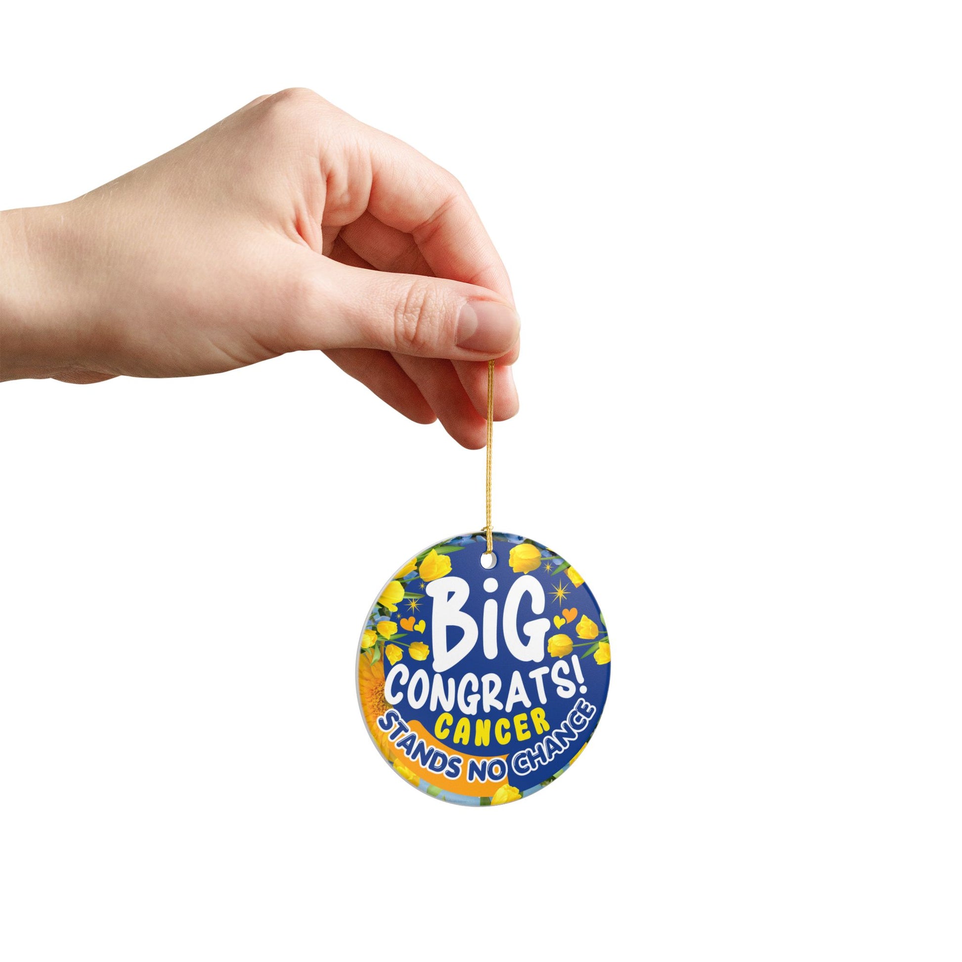 Cancer Victory Ceramic Ornament. Hand holding a round blue and yellow ornament with 'Big Congrats! Cancer Stands No Chance' text on a white background