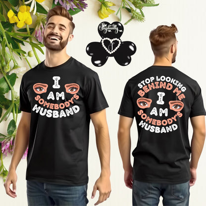 Black t-shirt with 'I AM SOMEBODY'S HUSBAND' text and eye graphics worn by a person, with a brand logo in the corner.