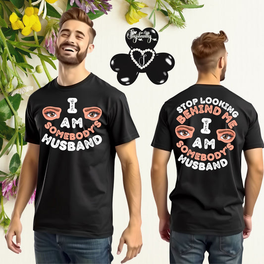 Black t-shirt with 'I AM SOMEBODY'S HUSBAND' text and eye graphics worn by a person, with a brand logo in the corner.