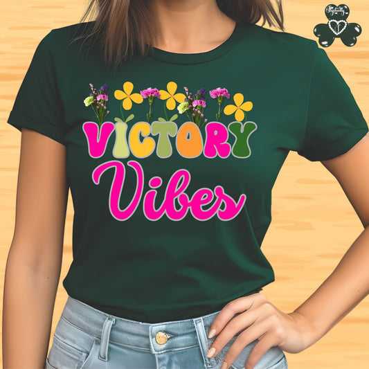 Motivational T-shirt for positive affirmations. Green t-shirt with 'Victory Vibes' text and flowers on a wooden surface