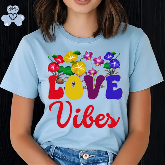 Motivational T-shirt for positive affirmations. Person wearing a light blue t-shirt with colorful floral design and 'Love Vibes' text on a black background.