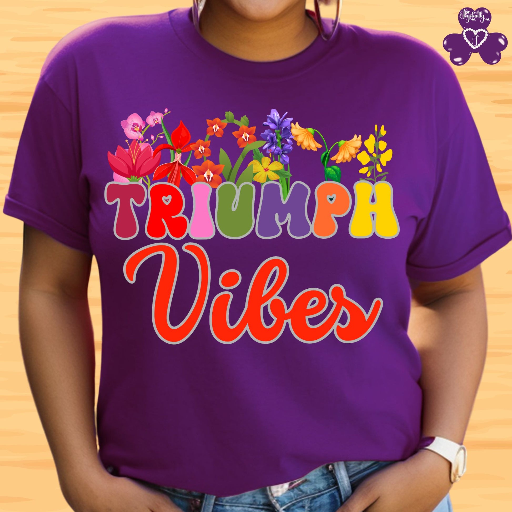 Motivational T-shirt for positive affirmations. Purple t-shirt with colorful floral design and 'TRIUMPH Vibes' text on a wooden background